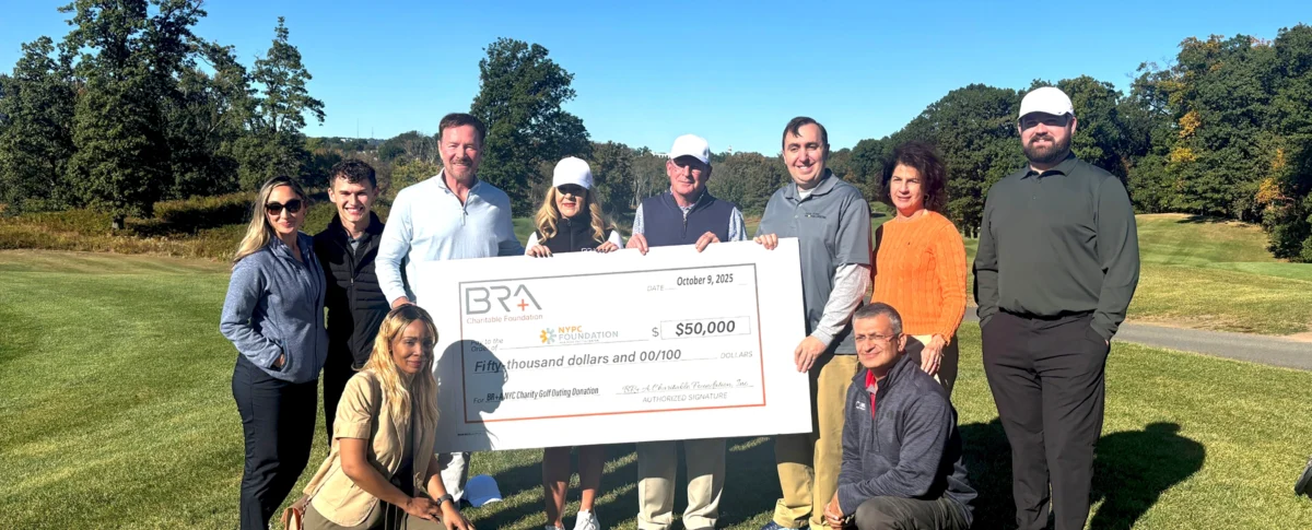 Team members from both the New York Proton Center and the BR+A Charitable Foundation stand outside on a sunny day, holding a large ceremonial check for their golf tournament fundraiser in support of the Forward Together program.