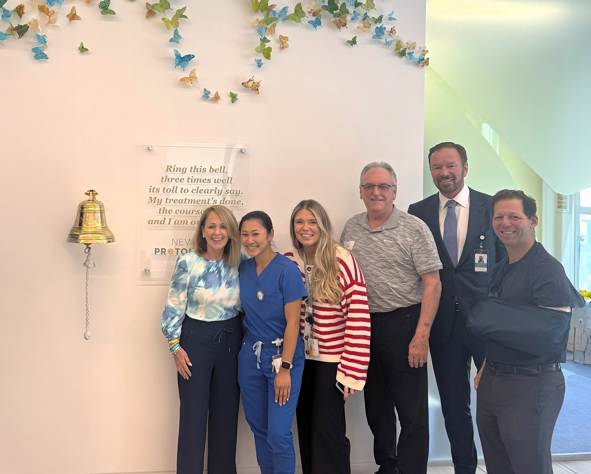 The New York Proton Center team posing with a patient next to the end of treatment bell.